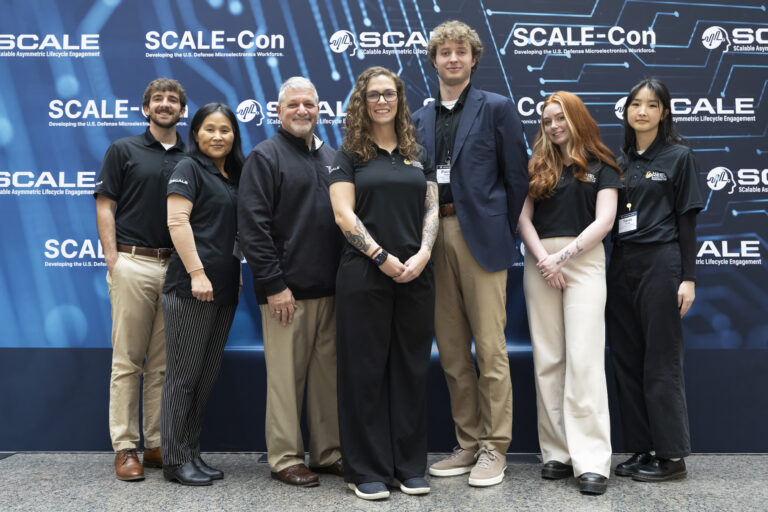 Eight people pose together at a conference in front of a blue SCALE-Con backdrop, smiling for the group photo.