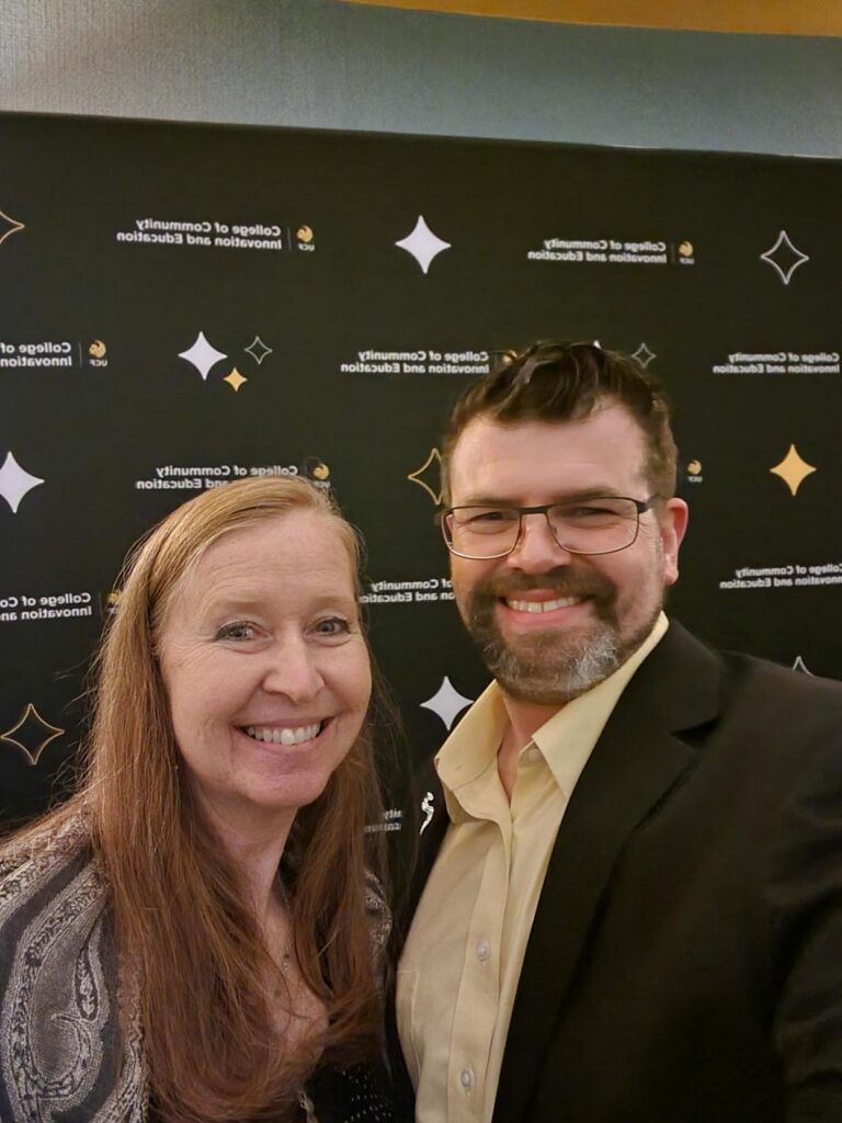 Smiling woman and man in business attire posing for a photo at a professional event, with a dark backdrop featuring star logos.