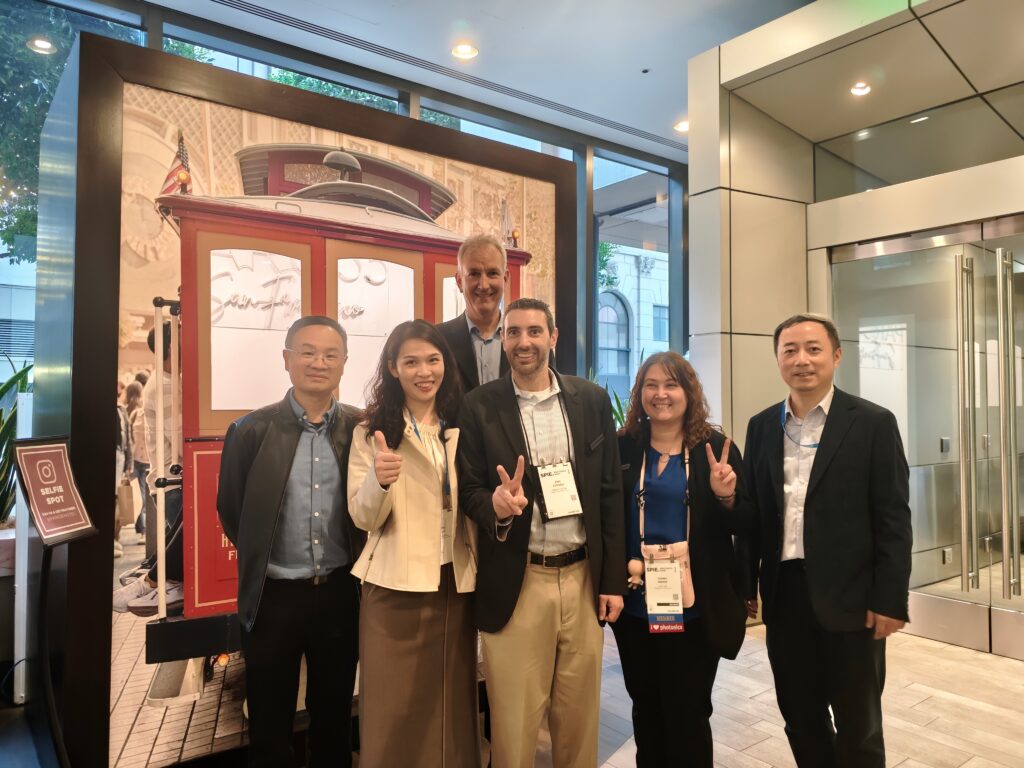 Group of five professionals posing for a photo in a modern lobby, smiling at the camera with a vintage red display behind them and a guest banner nearby.
